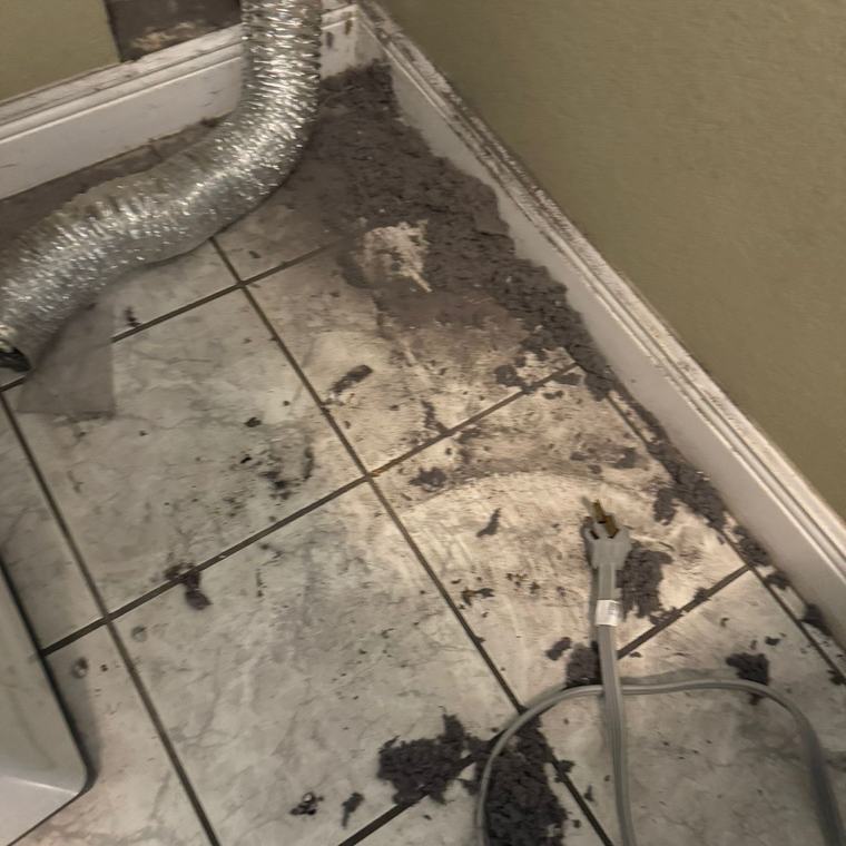 Lint and debris covering the floor behind a dryer